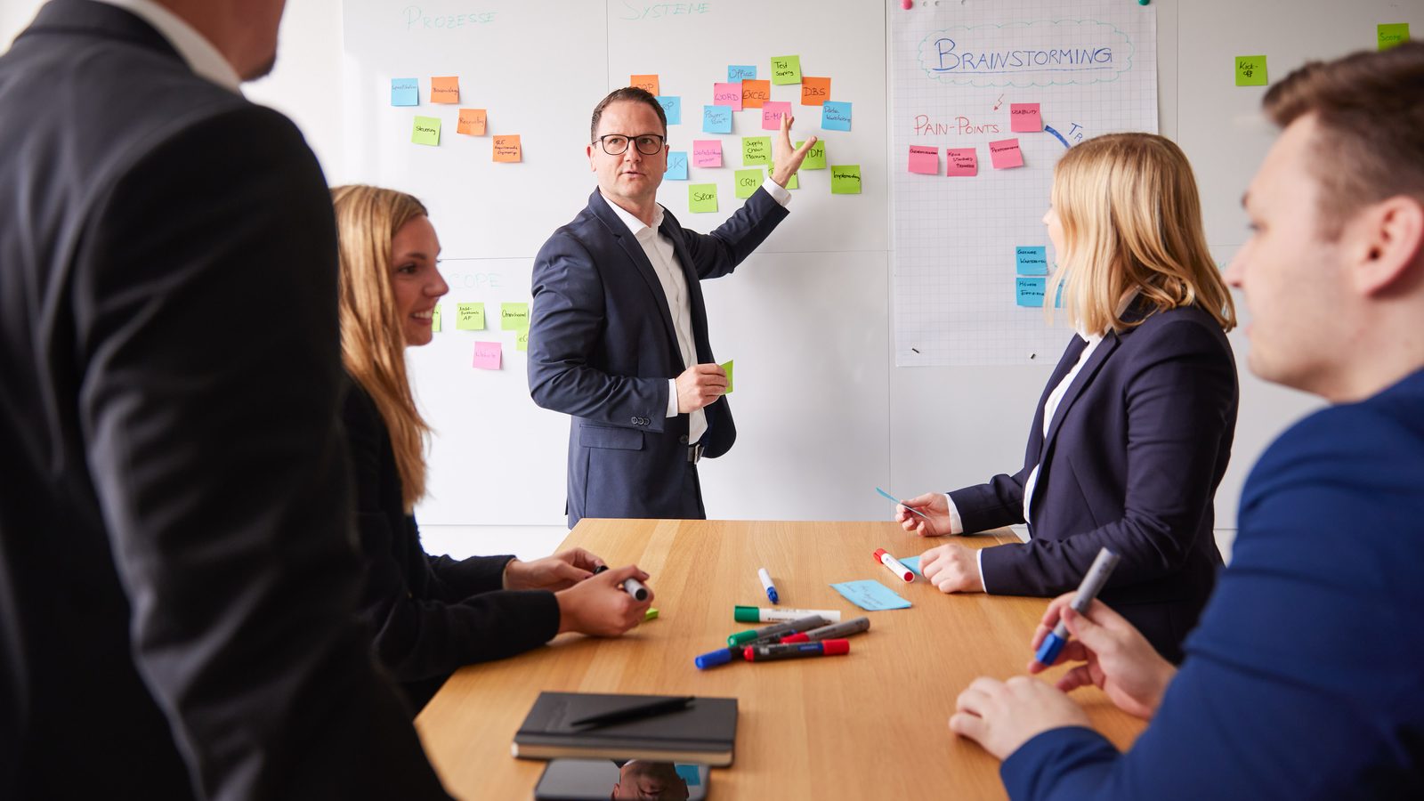 Workshop at ReqPOOL: a consultant explains the next decisions at a wall of sticky notes while the team sits at the table.