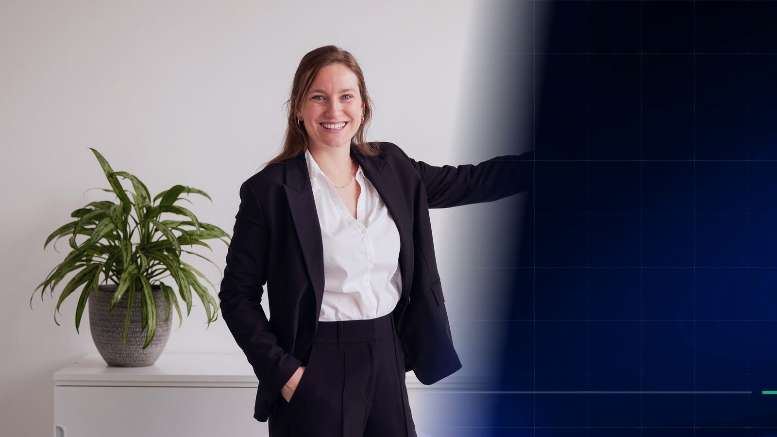 A ReqPOOL consultant stands in a bright office next to a green plant and gestures toward a dark blue surface with a fine grid.