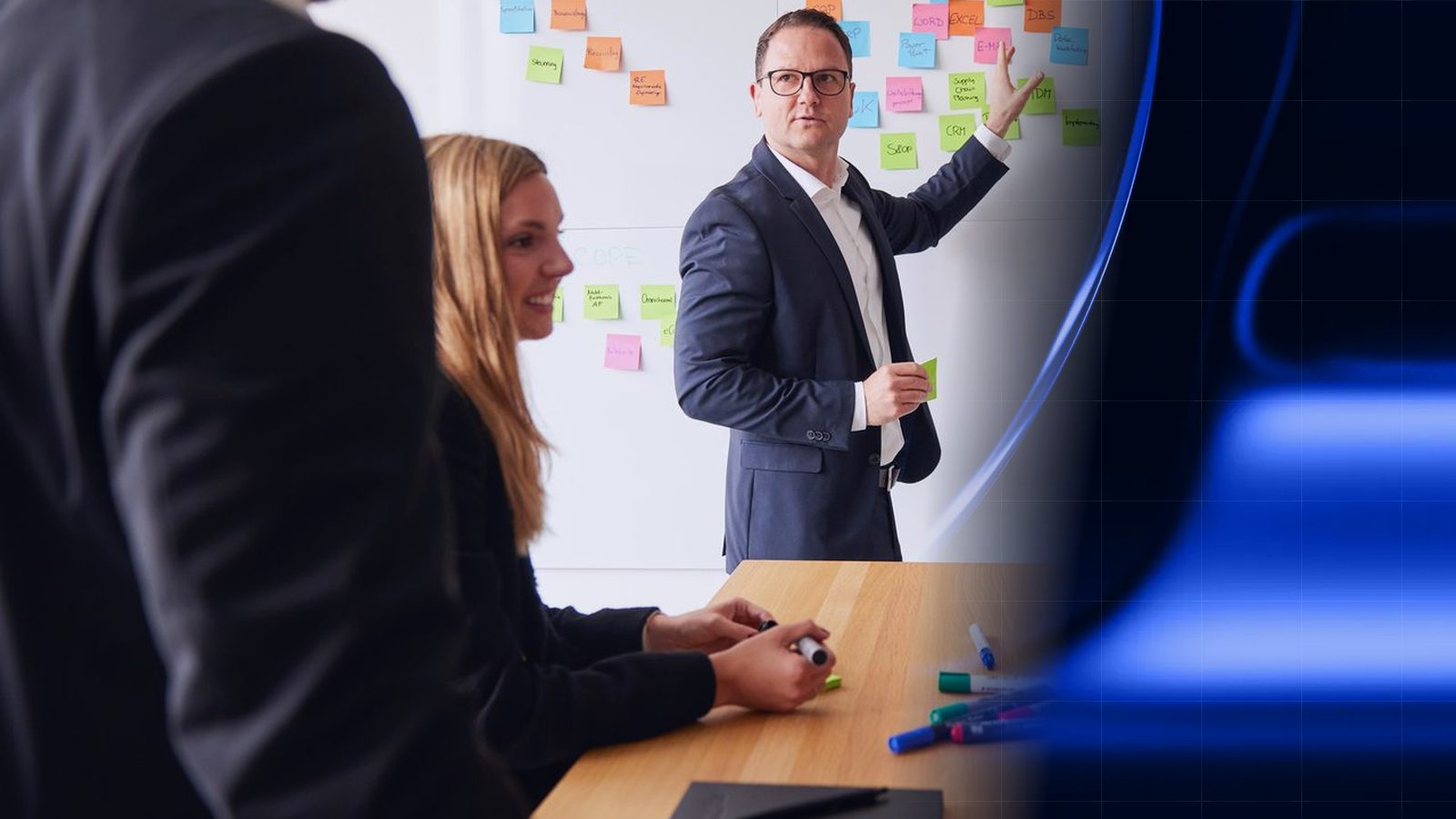 Workshop at ReqPOOL: a consultant explains a system landscape at a wall covered with sticky notes while two colleagues listen; on the right the image blends into a blue surface with grid lines.