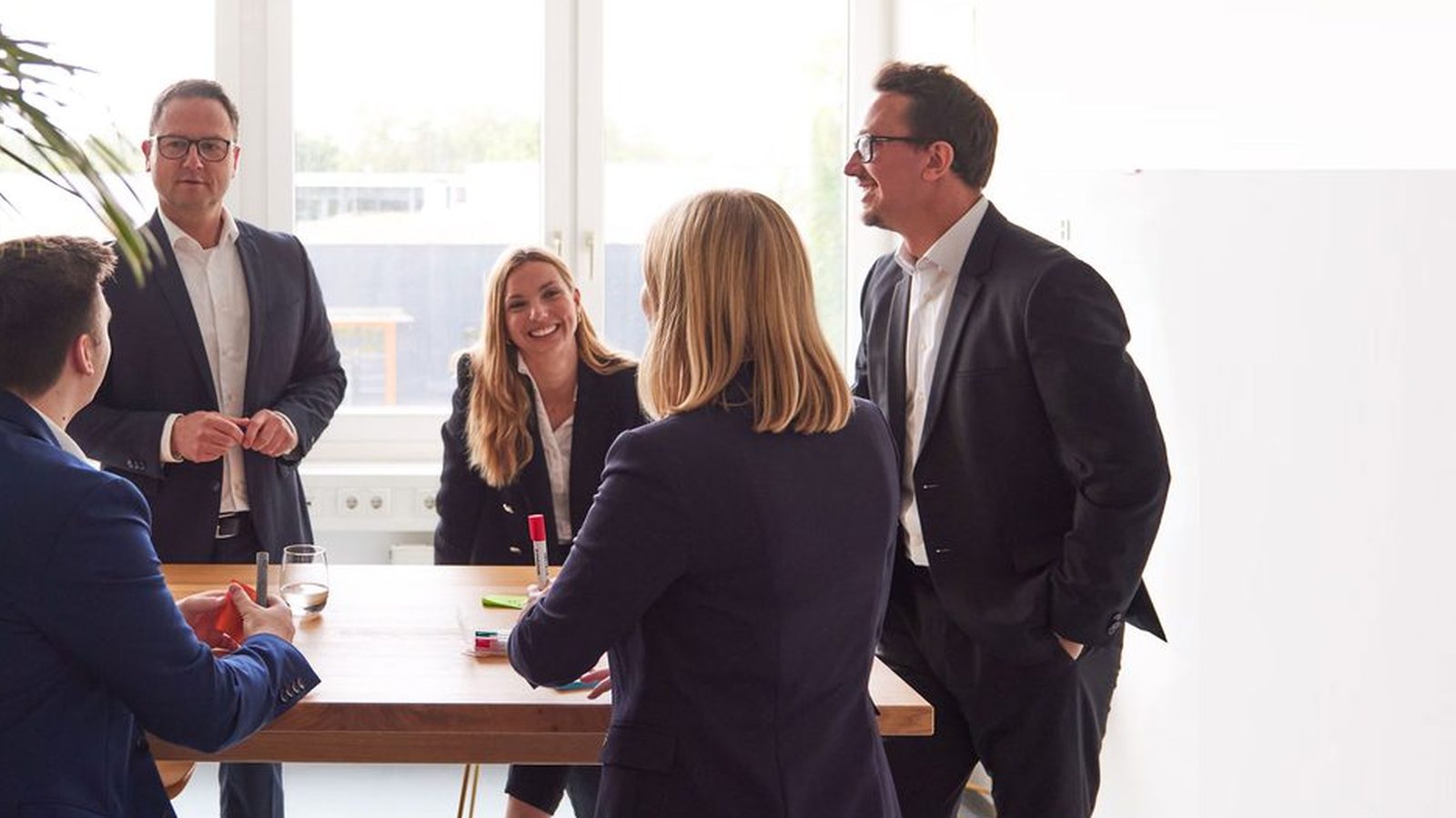Five ReqPOOL consultants discuss next steps around a wooden table in a bright office with a large screen.