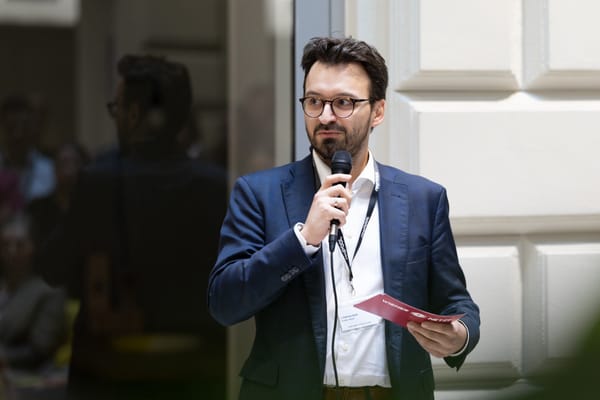 Speaker with glasses and a microphone holding a small red card