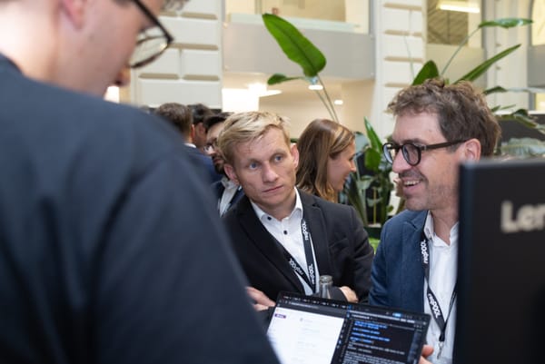 Two men talking at a table with a laptop, both smiling