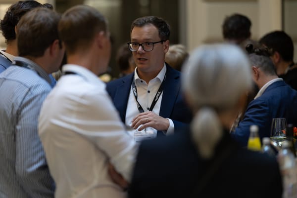 Man in a dark jacket talking with several guests in the event space