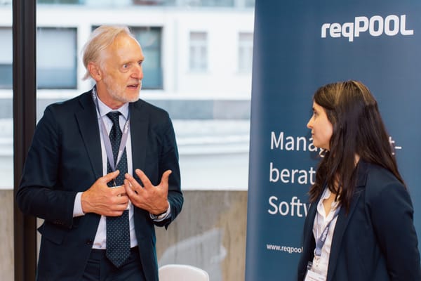 Guest gesturing in conversation in front of a ReqPOOL banner
