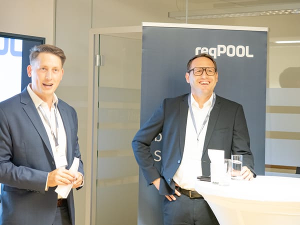 Two men in suits addressing the guests in front of a ReqPOOL banner