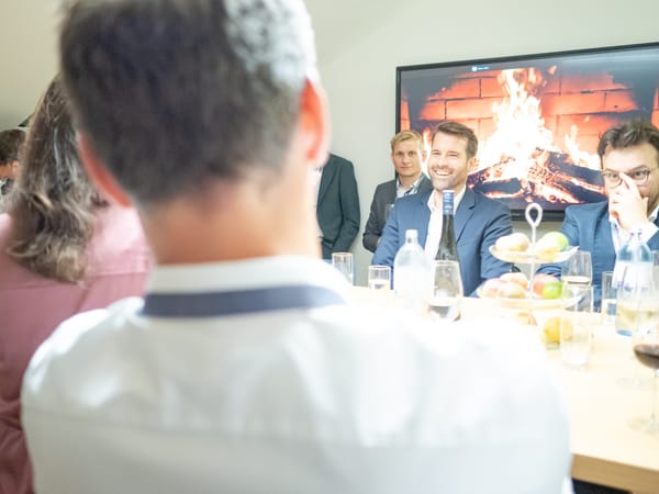Guests at a table with drinks and fruit, a fireplace video playing on the screen behind them