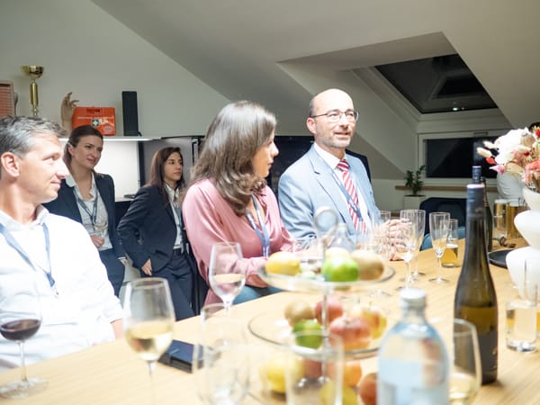 Guests in conversation at a long table with fruit, wine and water