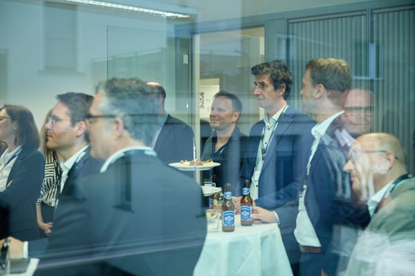Blick durch eine Glasscheibe auf Gäste an Stehtischen mit Getränken und Snacks