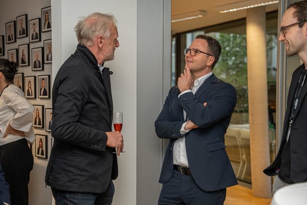 Two guests talking in the office, with a row of portrait photos on the wall