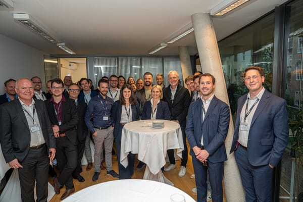 Large group of guests gathered around a standing table, looking at the camera