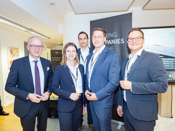 Five people in business attire posing in front of an event banner