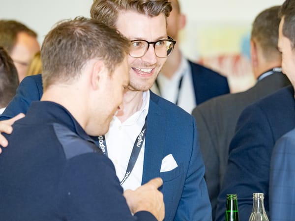 Two guests greeting each other warmly, one with an arm around the other’s shoulder