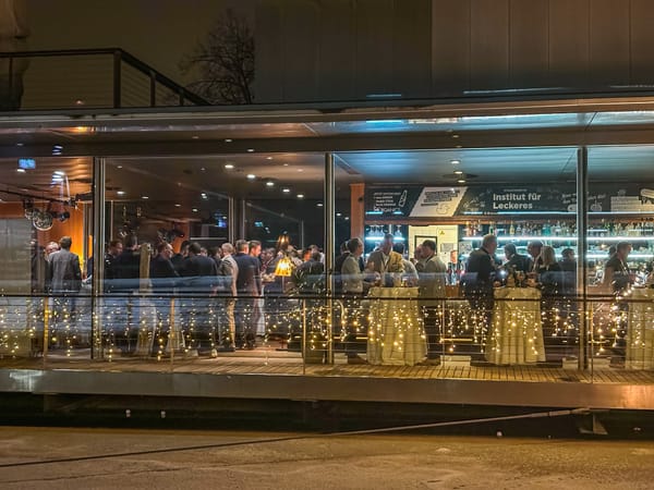Blick von außen durch die Glasfront auf den abendlich beleuchteten Veranstaltungsraum