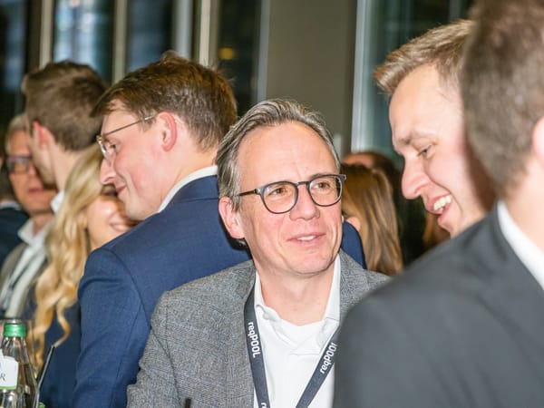 Gäste im Gespräch, im Vordergrund ein lachender Gast mit Brille