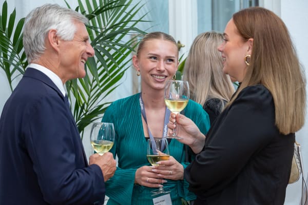 Three people with wine glasses laughing in conversation among houseplants