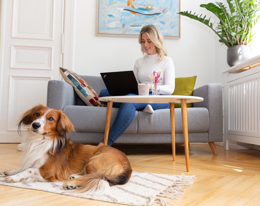 Blonde Frau mit Laptop auf Couch, Tisch, Hund